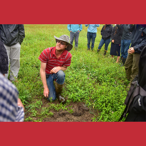 man crouching in field with people standing around him