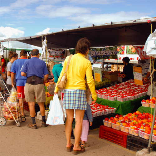 people standing in front of a food stand at an outdoor market